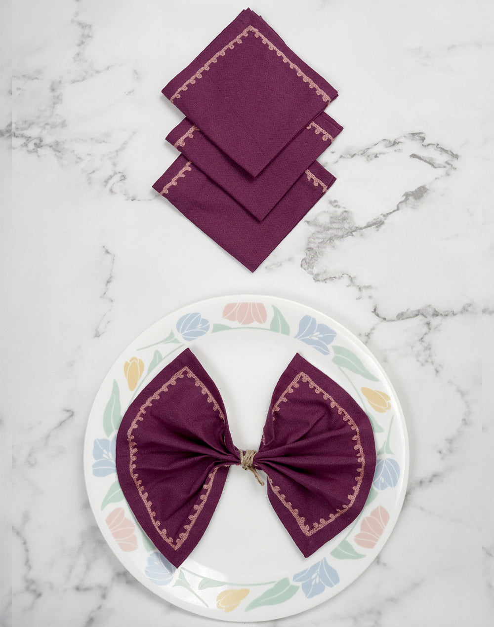 Set of purple napkins on a marble surface with a decorative plate featuring a purple bow.