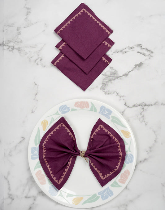 Set of purple napkins on a marble surface with a decorative plate featuring a purple bow.